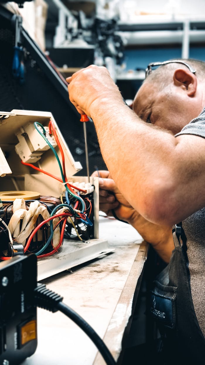 services-03 Expert electrician repairing an electrical device in a workshop setting, focusing on wiring.