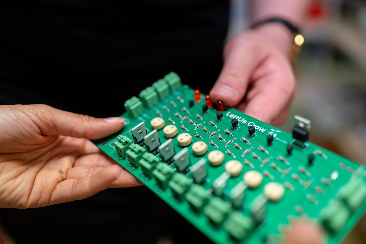 contact-img Close-up of hands holding a green circuit board used for electronic projects.